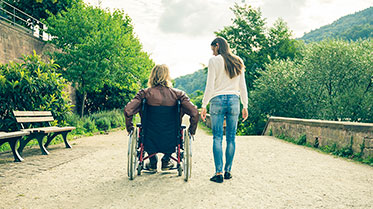 Vergrößerungsansichten für Bild: Foto: Eine Person im Rollstuhl und eine Frau gehen spazieren.